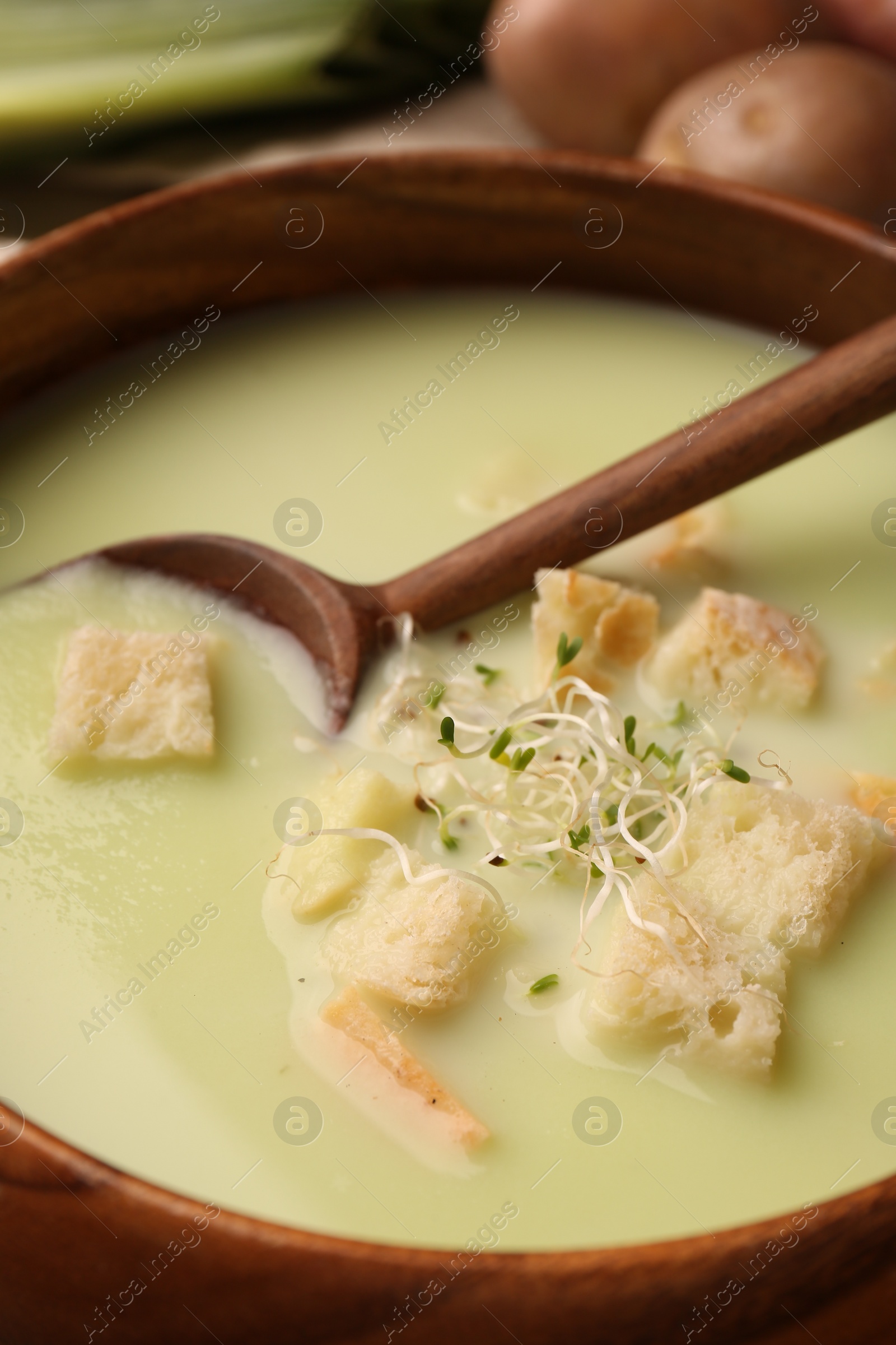Photo of Bowl of tasty leek soup with croutons and spoon on table, closeup