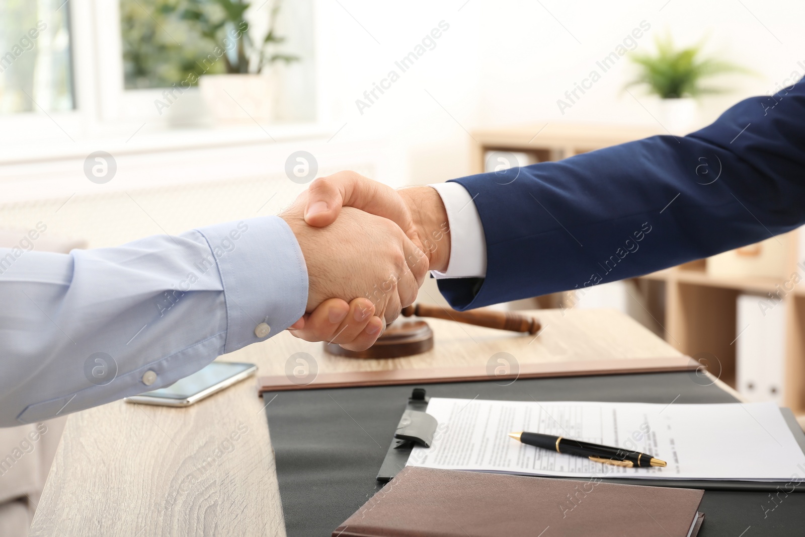 Photo of Lawyer handshaking with client over table in office, closeup