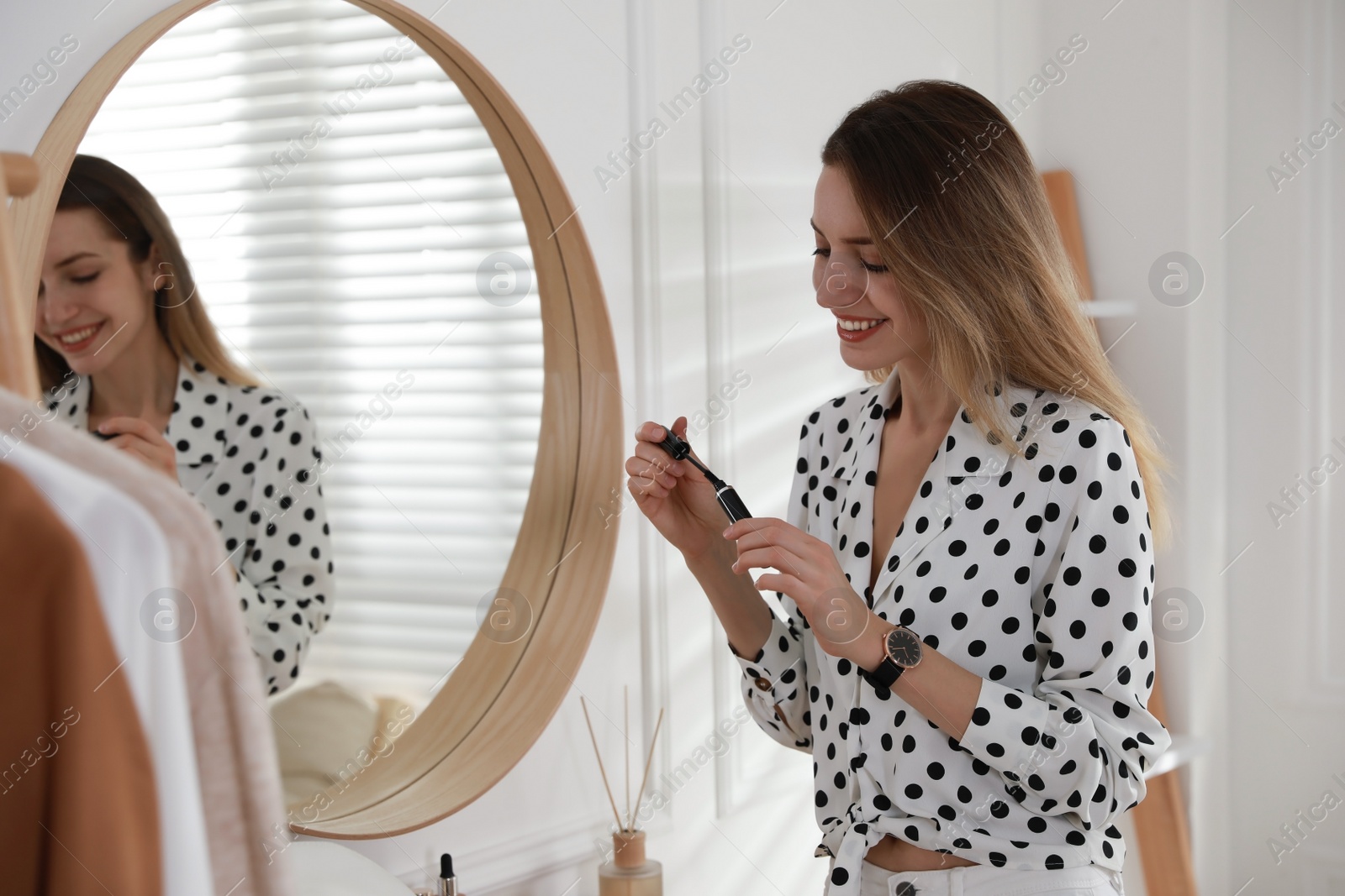 Photo of Young woman doing makeup near mirror at home. Morning routine
