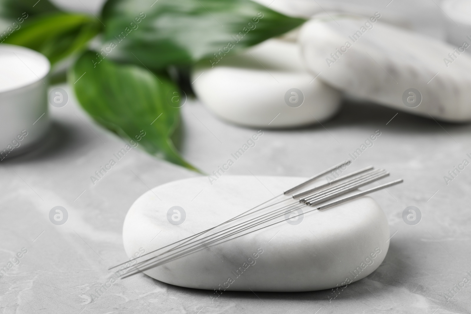 Photo of Stone with acupuncture needles on light grey marble table
