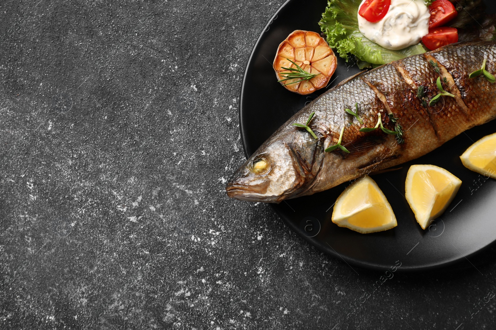 Photo of Plate with delicious sea bass fish and ingredients on dark grey table, top view. Space for text