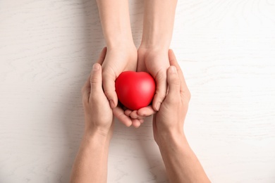 People holding red heart on wooden background, top view. Cardiology concept