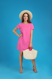 Young woman with stylish straw bag on light blue background