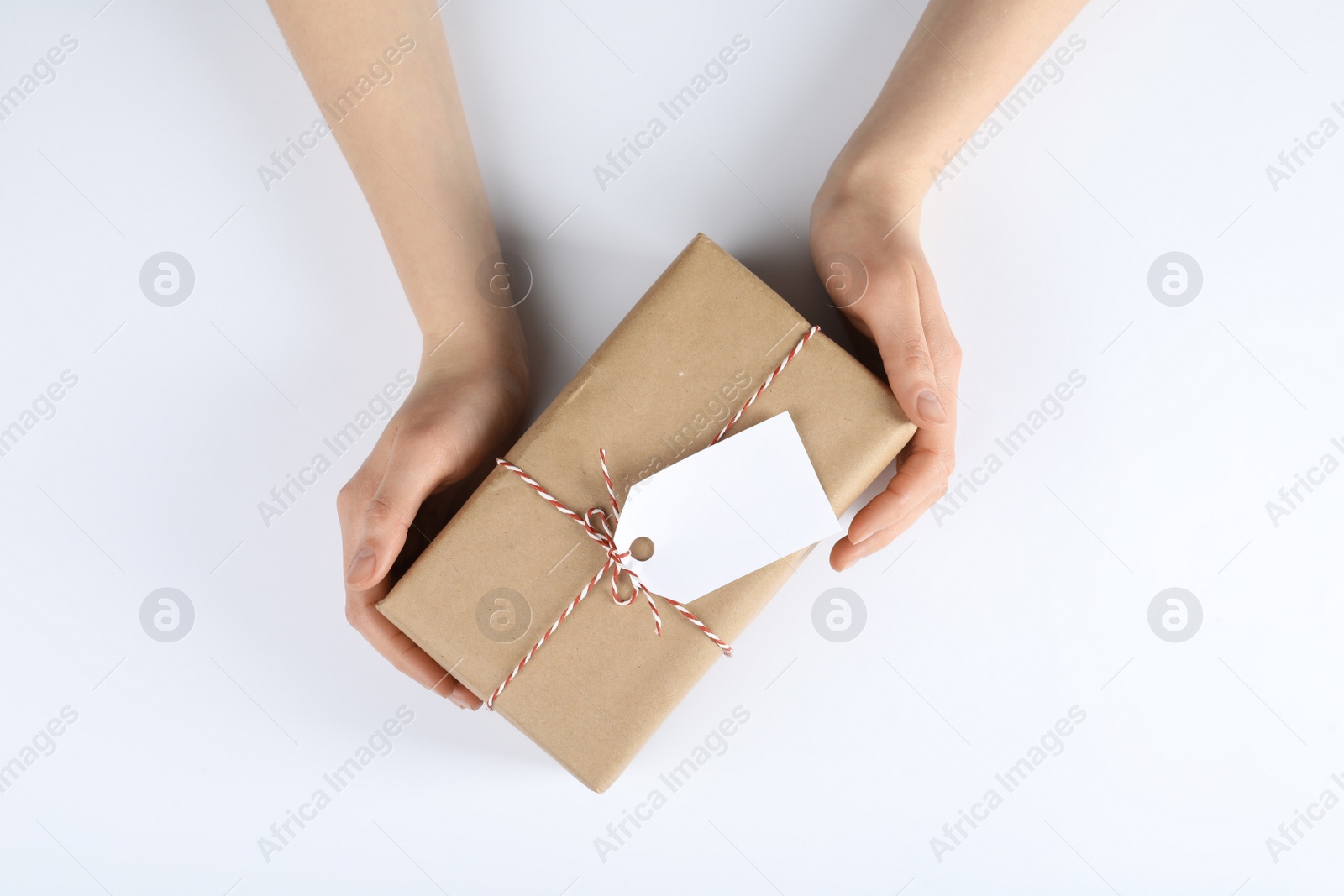 Photo of Woman holding parcel wrapped in kraft paper with tag on white background, top view