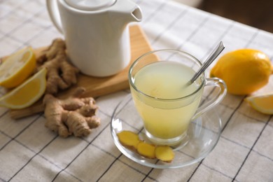 Photo of Glass of aromatic ginger tea and ingredients on white checkered tablecloth, space for text