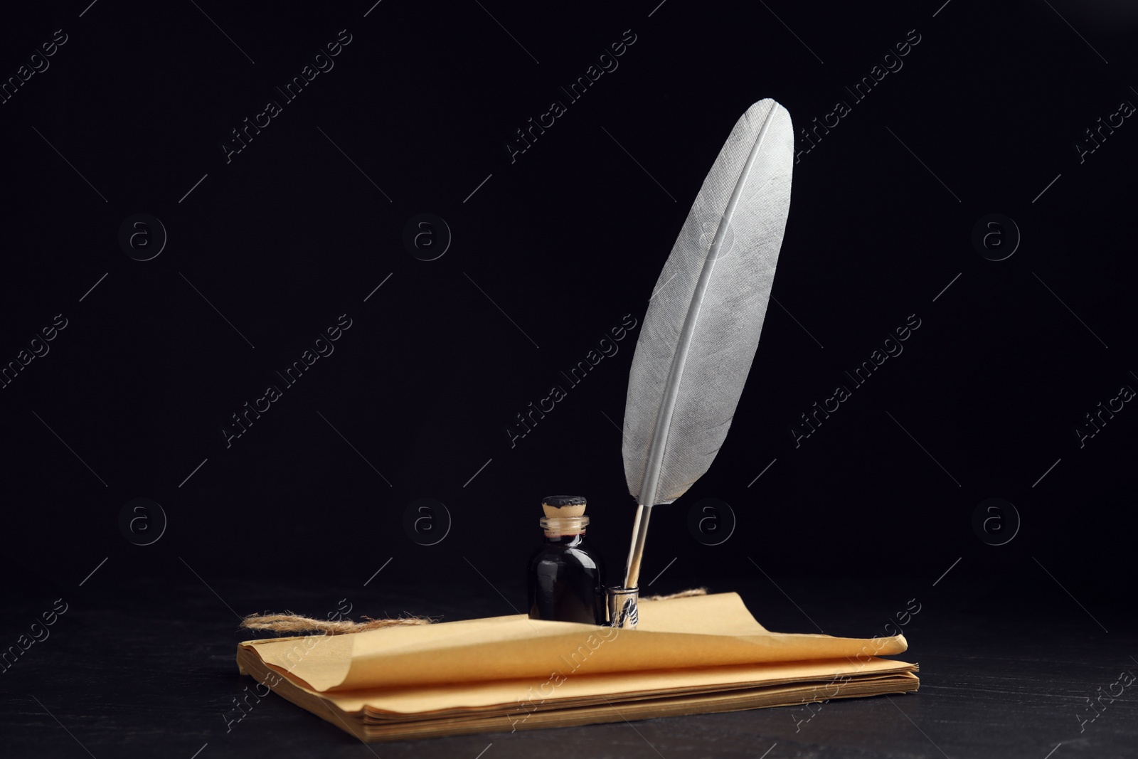 Photo of Feather pen, bottle of ink and old paper on black table