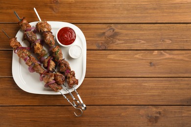 Photo of Metal skewers with delicious meat, ketchup and sauce served on wooden table, top view. Space for text