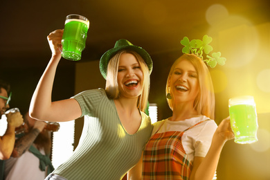 Young women with glasses of green beer in pub. St. Patrick's Day celebration