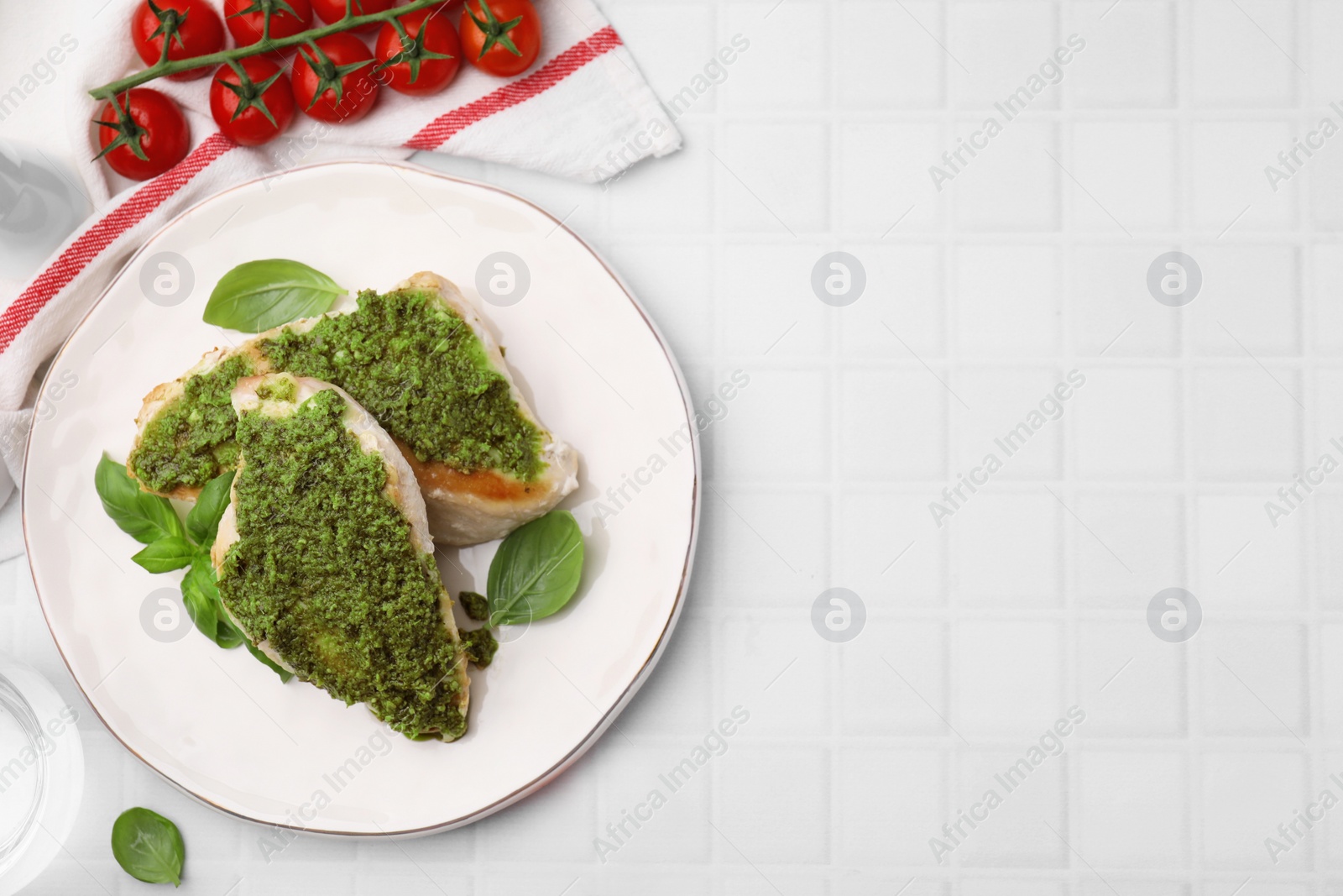 Photo of Delicious chicken breasts with pesto sauce, basil and tomatoes on white tiled table, flat lay. Space for text