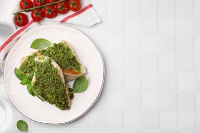 Delicious chicken breasts with pesto sauce, basil and tomatoes on white tiled table, flat lay. Space for text