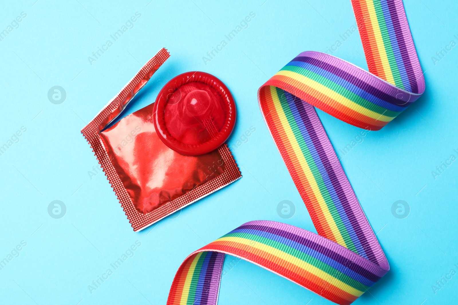 Photo of Red condom and rainbow ribbon on light blue background, flat lay. LGBT concept
