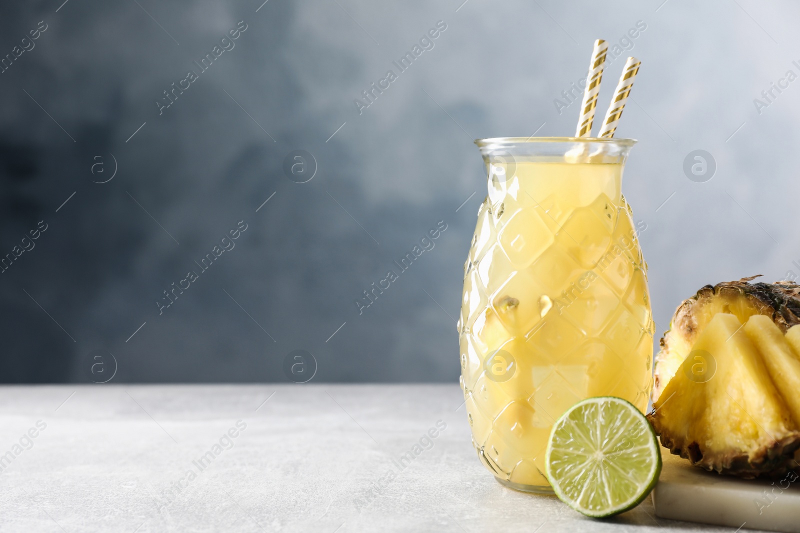 Photo of Delicious pineapple juice and fresh fruits on light grey table, space for text
