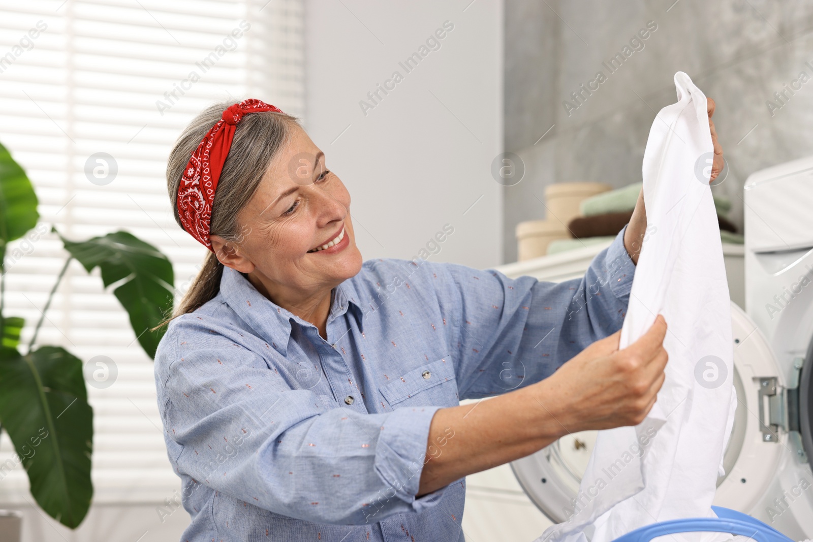 Photo of Happy housewife with laundry near washing machine at home