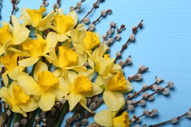 Bouquet of beautiful yellow daffodils and willow flowers on light blue wooden table, top view