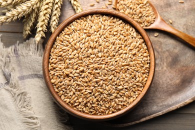 Photo of Wheat grains in bowl, spoon and spikes on wooden table, flat lay