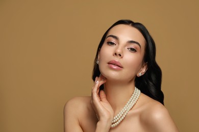 Young woman wearing elegant pearl jewelry on brown background, space for text