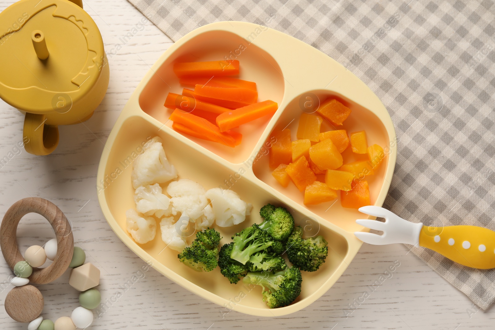 Photo of Baby food. Section plate with different vegetables on white wooden table, flat lay