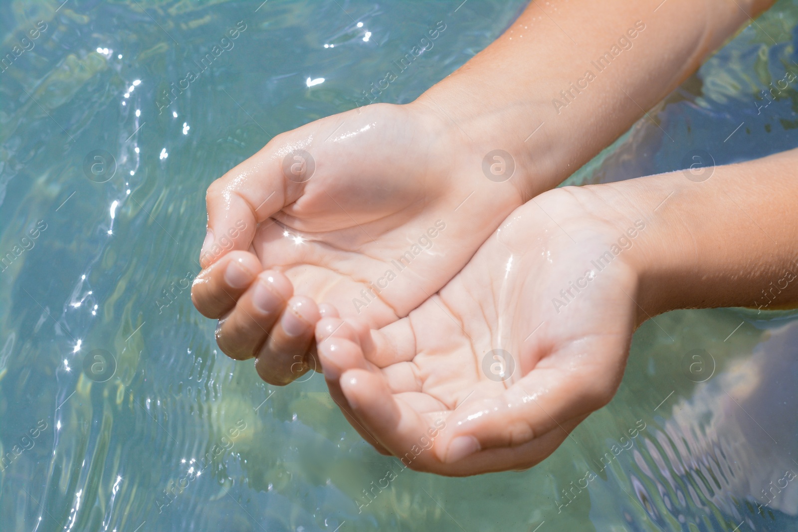 Photo of Kid holding water in hands above sea outdoors, closeup