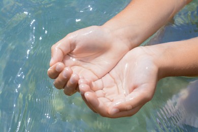 Kid holding water in hands above sea outdoors, closeup