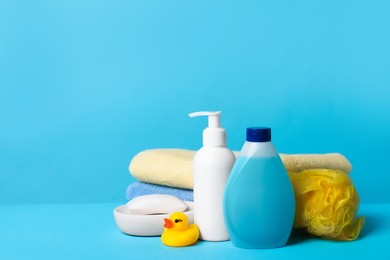 Photo of Baby cosmetic products, bath duck, sponge and towels on light blue background. Space for text