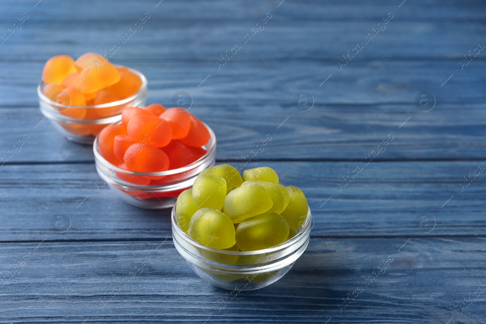 Photo of Glass bowls with tasty jelly candies on blue wooden table, space for text