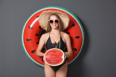 Photo of Beautiful young woman in bikini with inflatable ring and watermelon against dark background