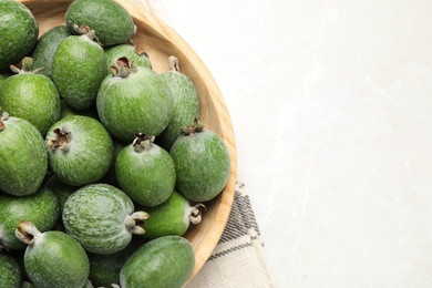 Photo of Fresh green feijoa fruits in bowl on light table, top view. Space for text