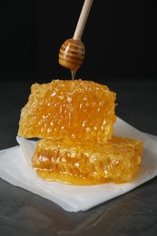 Photo of Dripping tasty honey from dipper onto honeycombs on dark table against black background