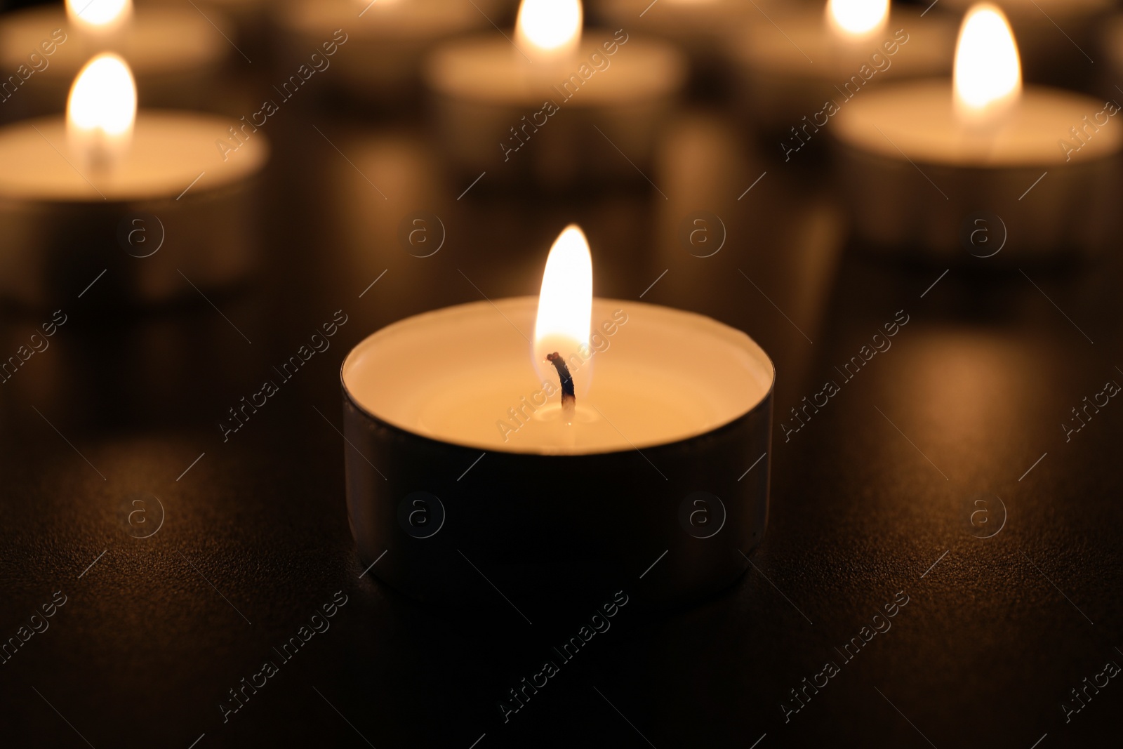 Photo of Burning candle on table in darkness, closeup. Funeral symbol