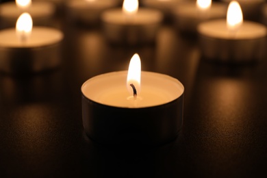 Burning candle on table in darkness, closeup. Funeral symbol