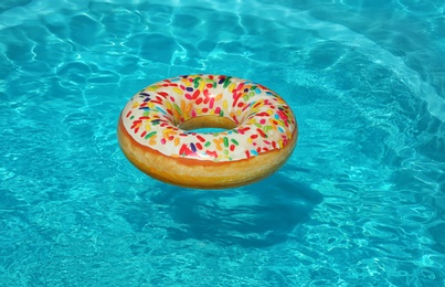 Bright inflatable doughnut ring floating in swimming pool on sunny day