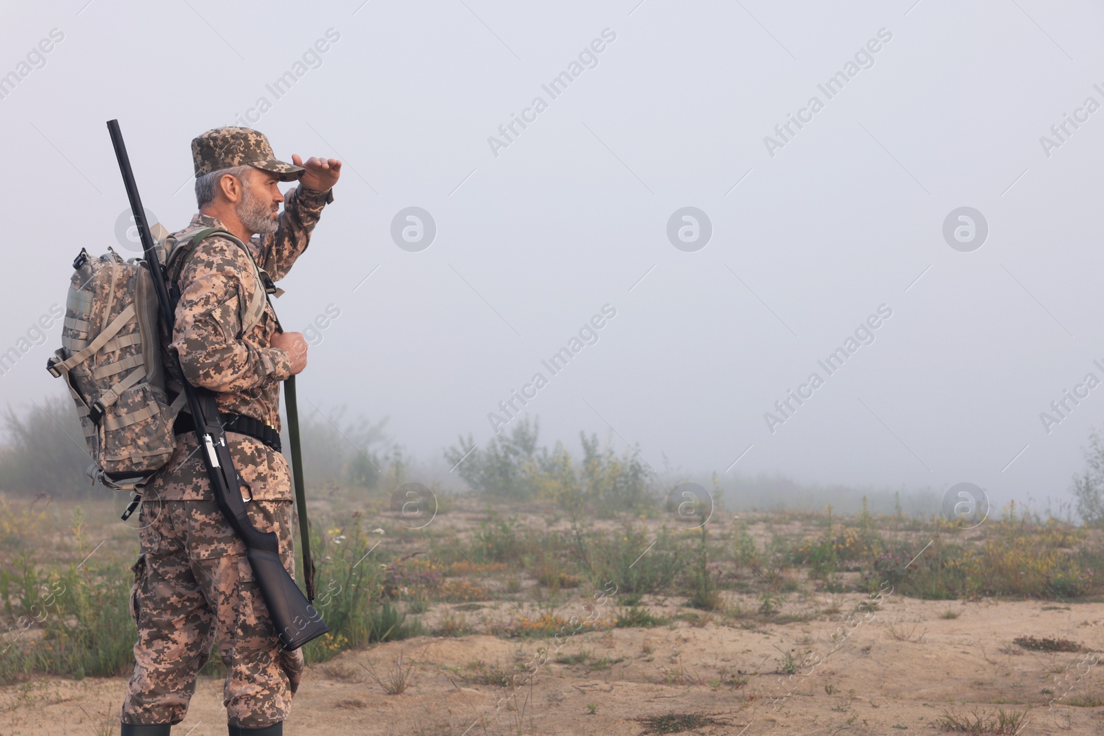 Photo of Man wearing camouflage with hunting rifle and backpack outdoors. Space for text