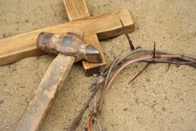 Photo of Crown of thorns, wooden cross and hammer on sand. Easter attributes