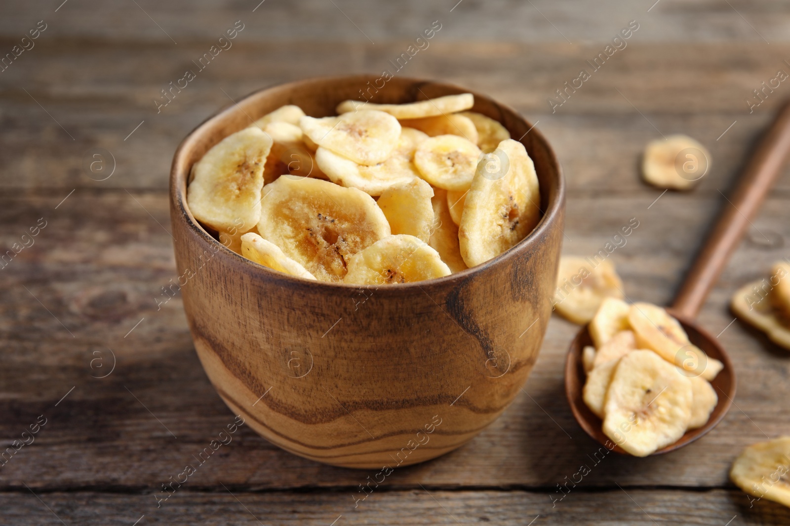 Photo of Bowl and spoon with sweet banana slices on wooden table. Dried fruit as healthy snack