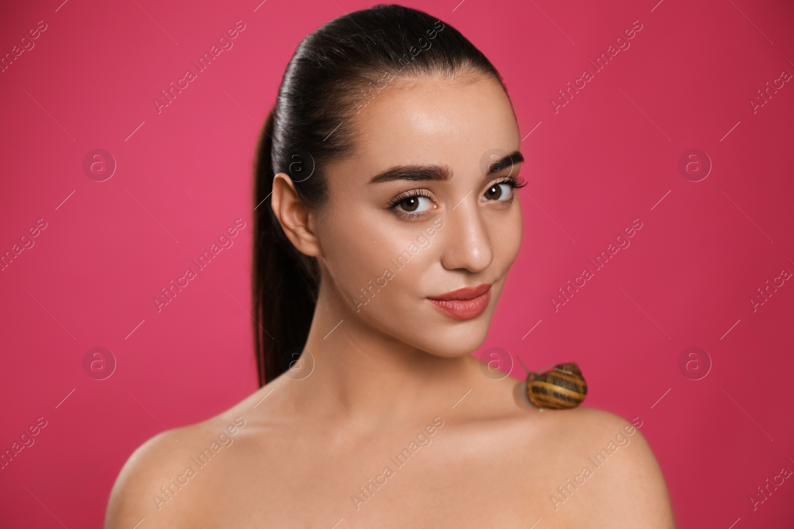 Photo of Beautiful young woman with snail on her shoulder against pink background