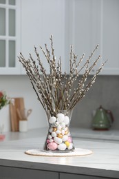 Vase with beautiful pussy willow branches and painted eggs on table in kitchen. Easter decor