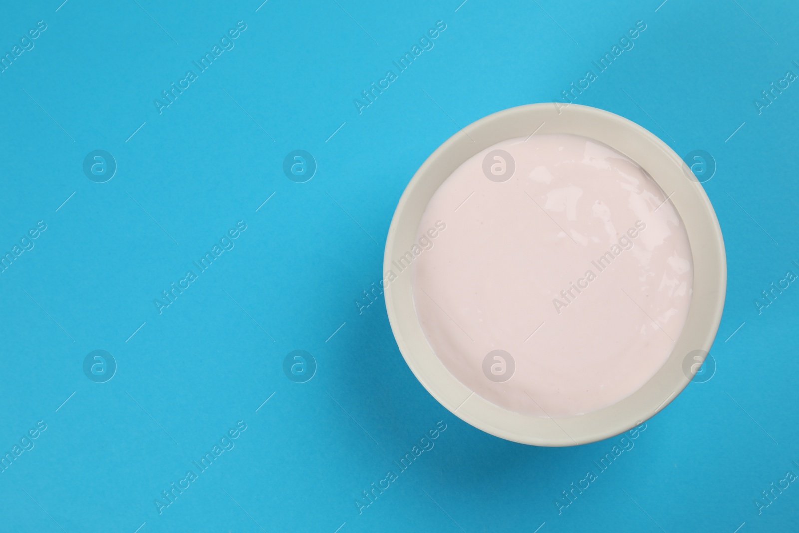 Photo of Bowl of tasty organic yogurt on light blue background