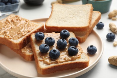 Photo of Delicious toasts with peanut butter and blueberries on white table, closeup