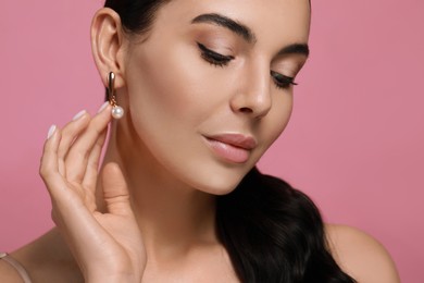 Young woman wearing elegant pearl earrings on pink background, closeup