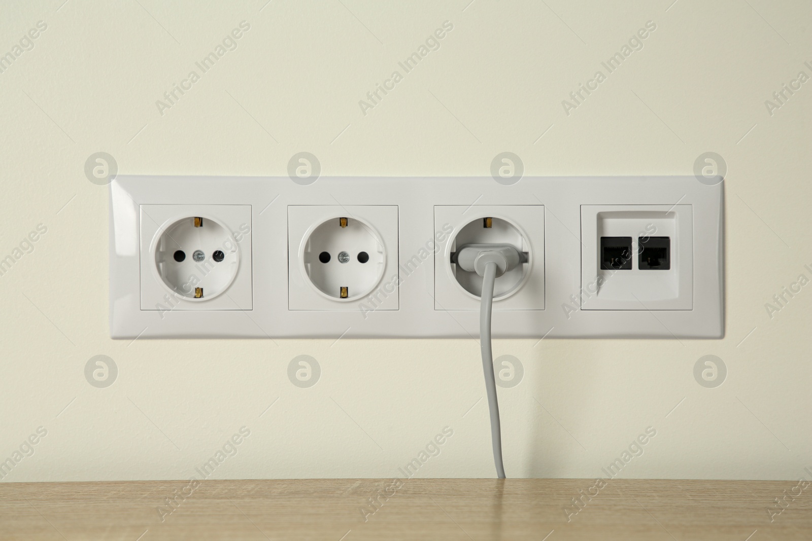 Photo of Many power sockets with plug and ethernet plate on white wall indoors