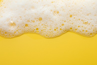 Photo of Fluffy soap foam on yellow background, top view. Space for text