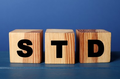 Photo of Wooden cubes with letters STD (sexually transmitted diseases) on blue table
