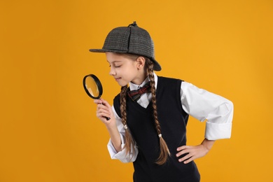 Photo of Cute little detective with magnifying glass on yellow background