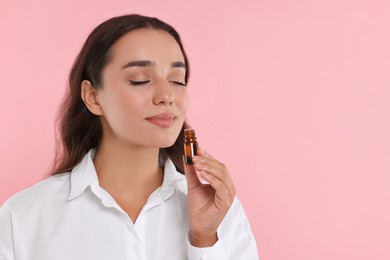 Photo of Beautiful young woman with bottle of essential oil on pink background, space for text