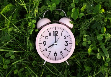 Photo of Pink small alarm clock on green grass outdoors, top view