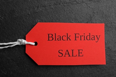 Photo of Red tag with words BLACK FRIDAY SALE on dark slate background, top view