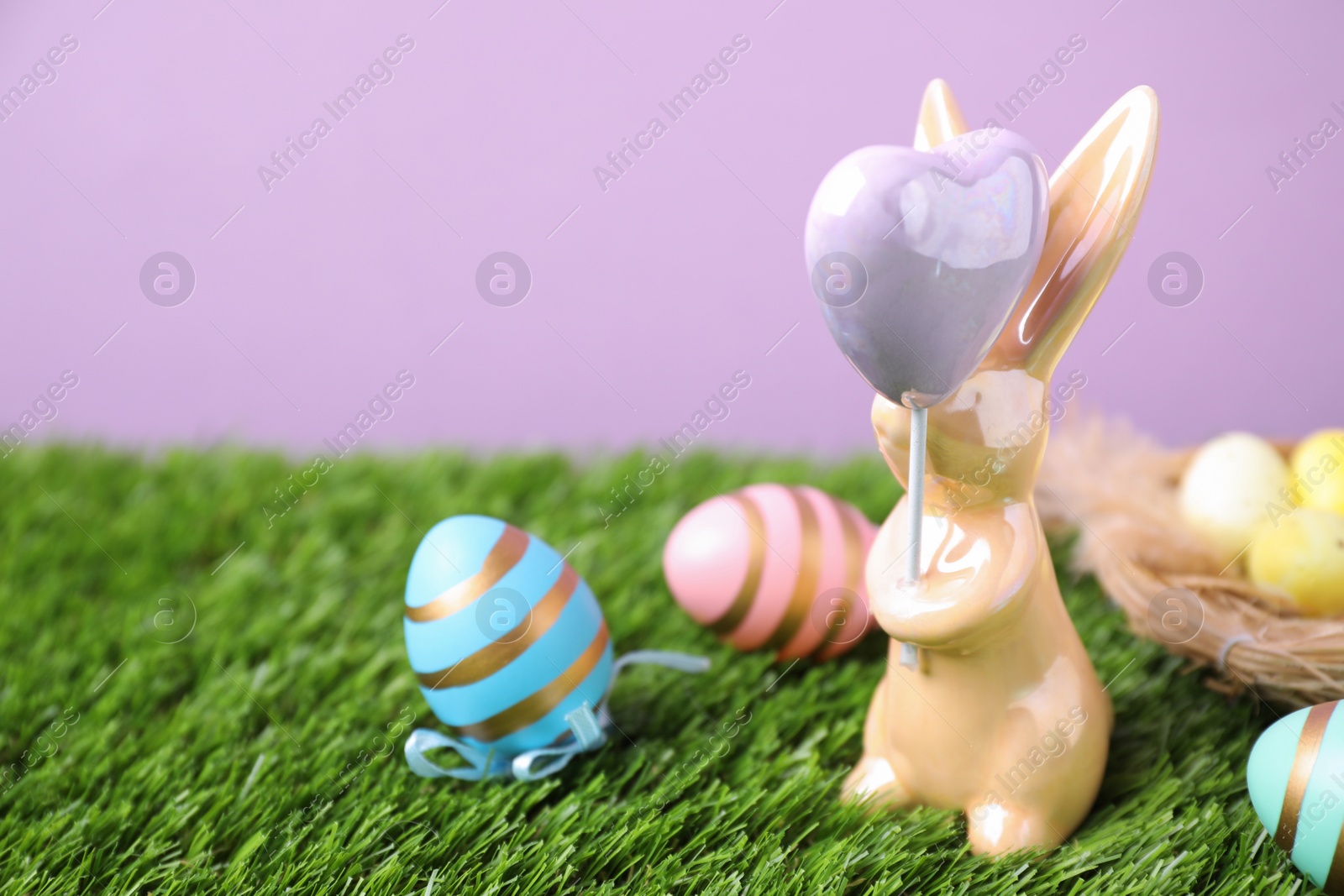 Photo of Easter bunny figure and dyed eggs on green grass against violet background. Space for text