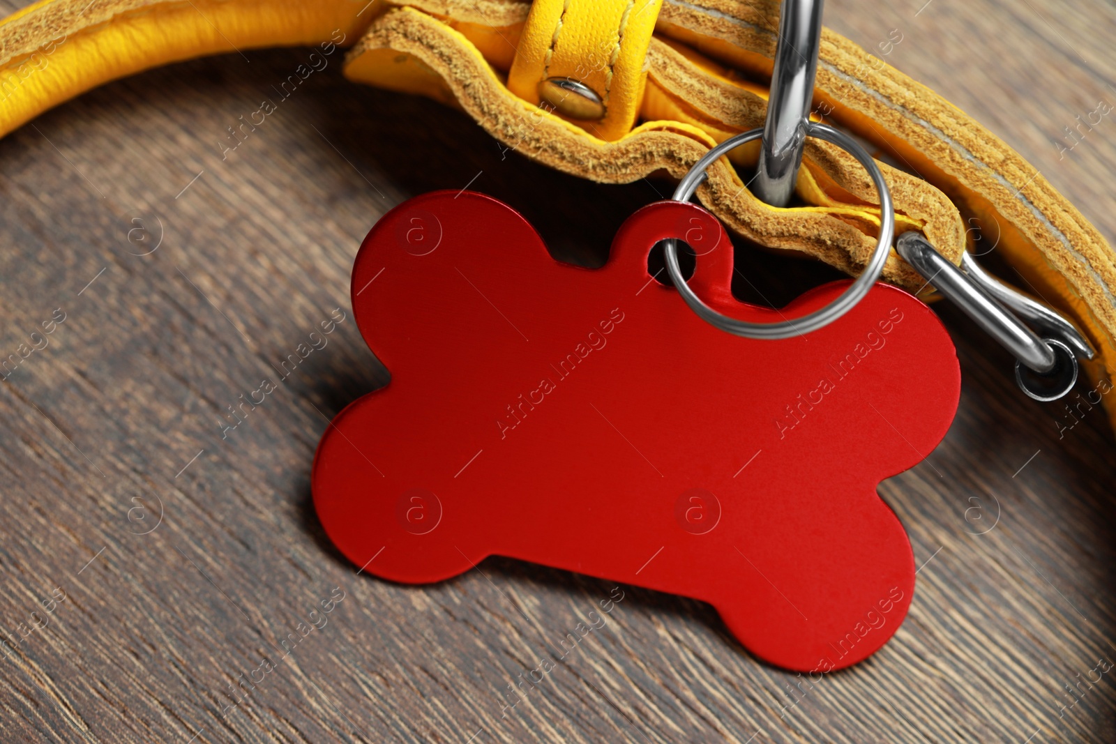 Photo of Yellow leather dog collar with red tag in shape of bone on wooden table, closeup. Space for text