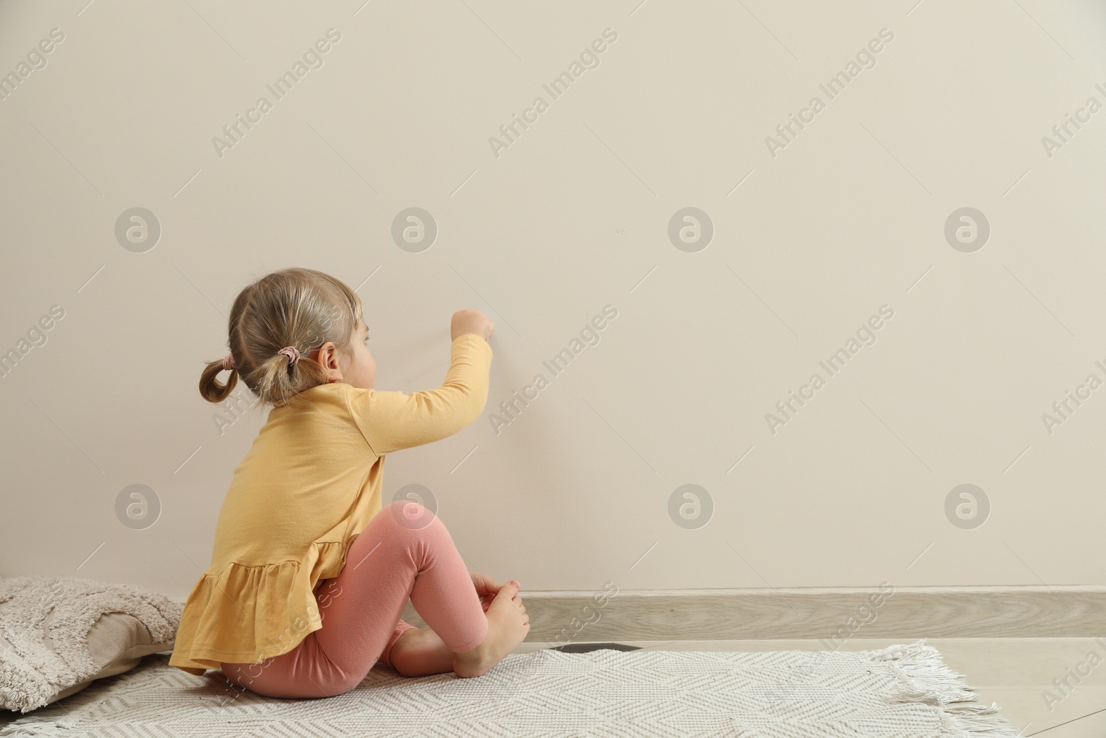 Photo of Little girl drawing on beige wall indoors, space for text. Child`s art