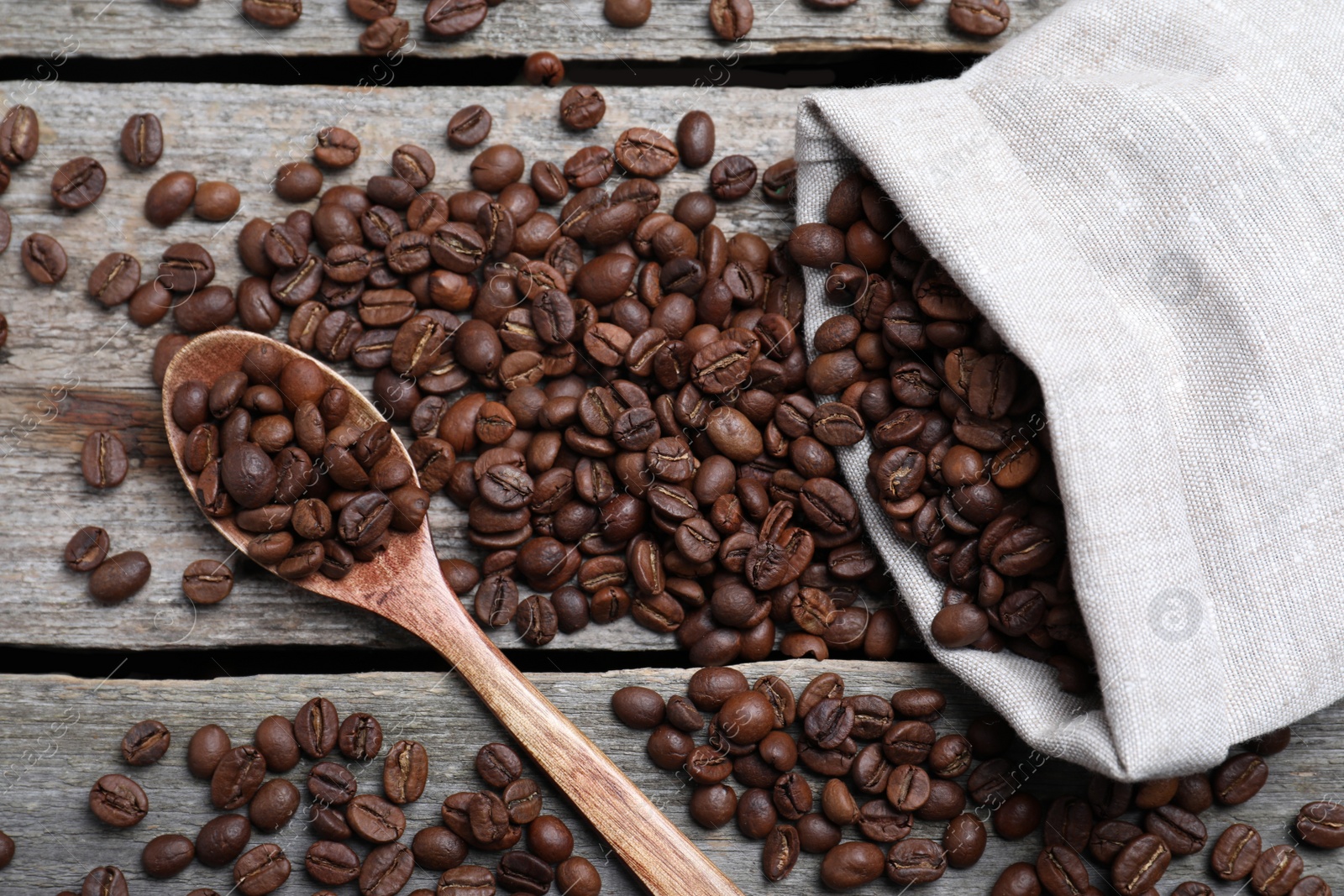 Photo of Bag and spoon with roasted coffee beans on wooden table, flat lay